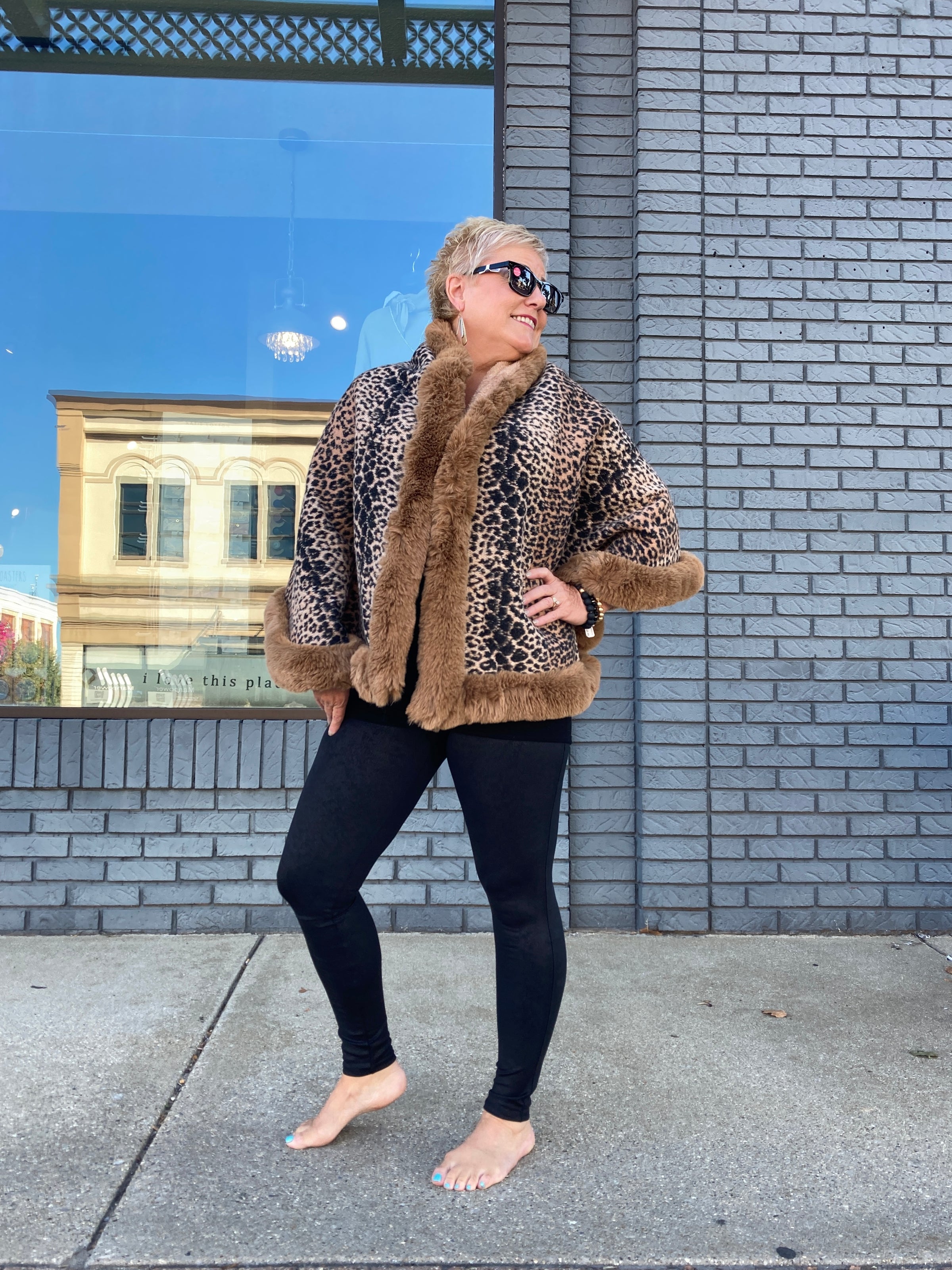 A fabulous looking woman wearing black leggings and a stunning leopard print kimono jacket with brown faux fur lining