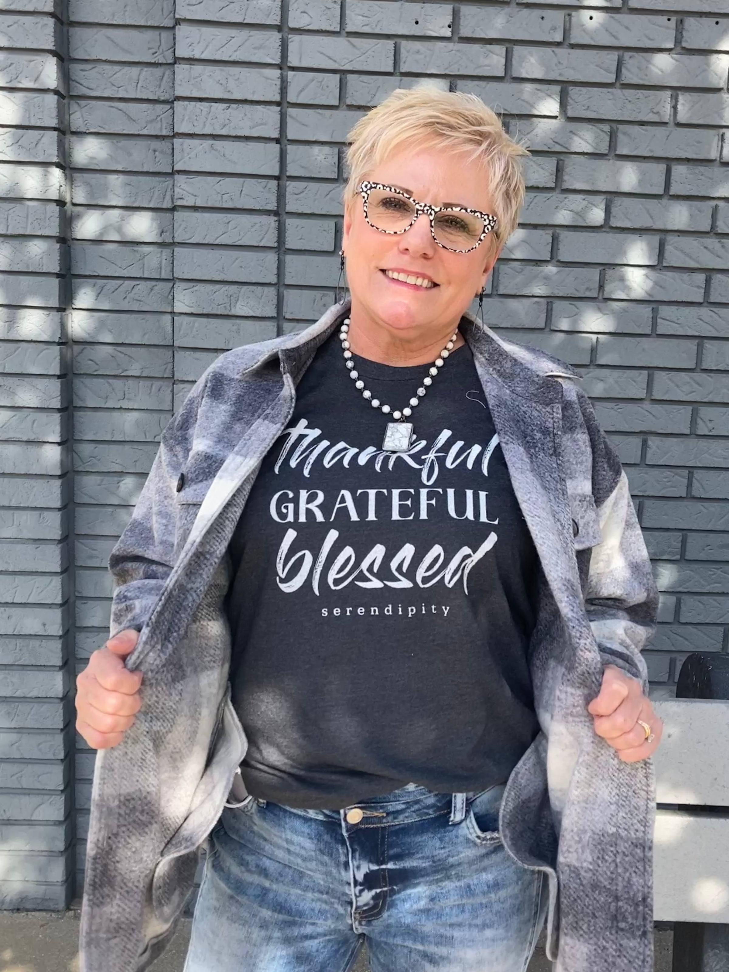 Woman Wearing a grey "thankful, grateful, blessed" graphic shirt with a grey flannel shacket over it.