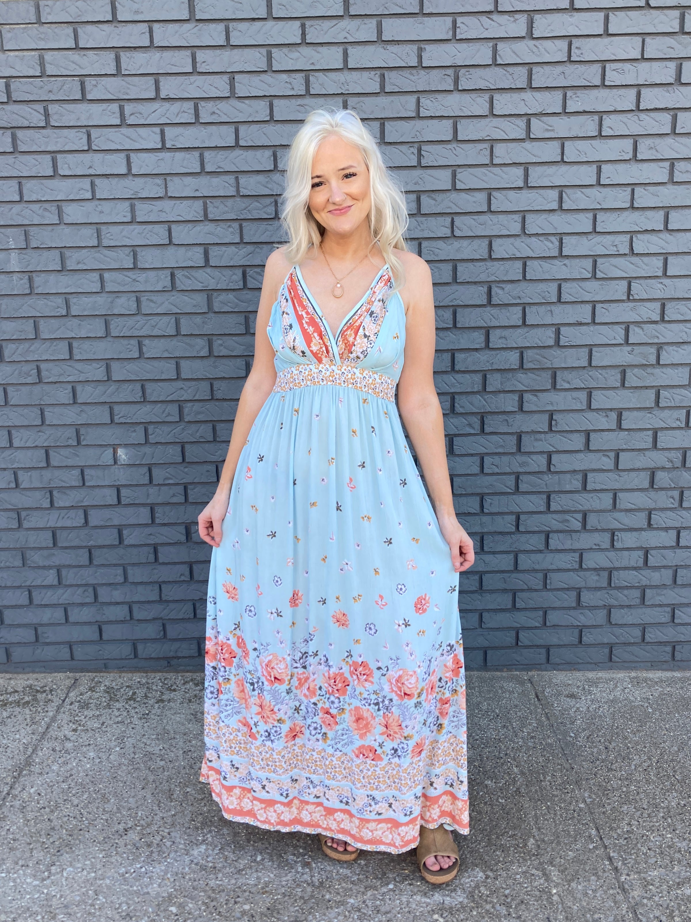a young woman in her 30s wearing a romantic blue maxi dress with a pink floral print.