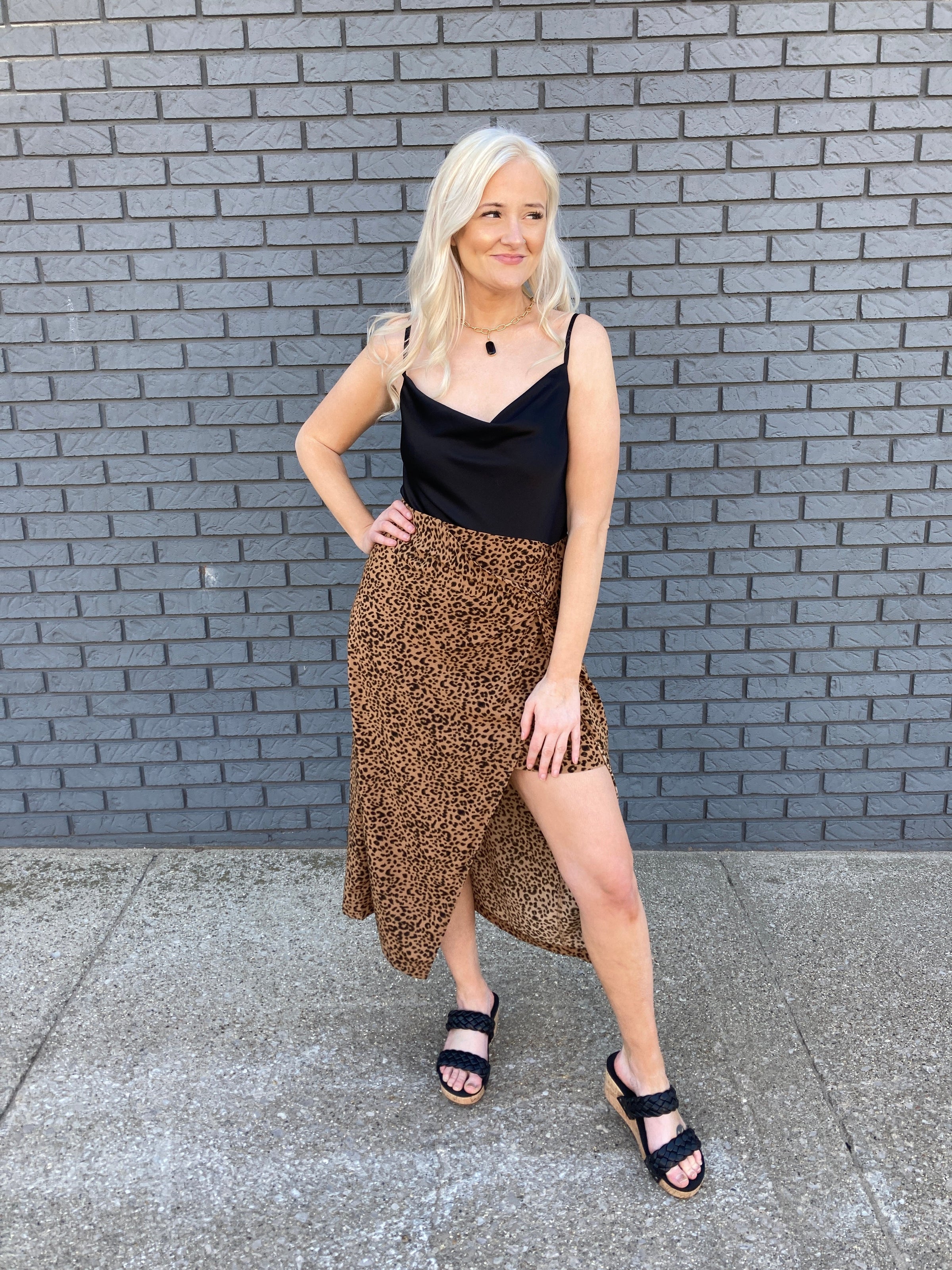 A young woman in her 30s wearing a black tank blouse and an animal print maxi skirt. 