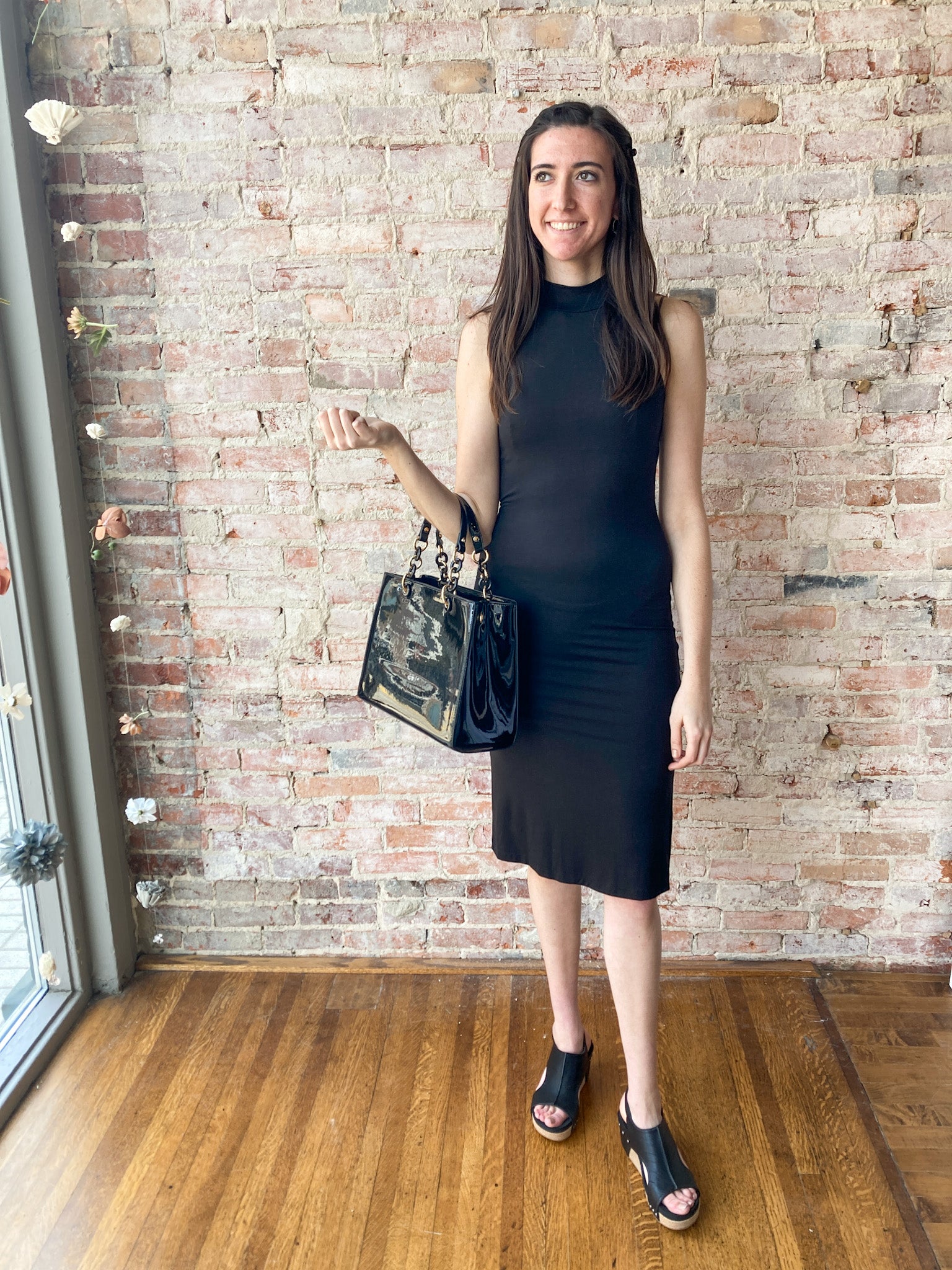 a beautiful woman wearing a tight little black midi dress. She is also wearing black platform shoes and carrying a black paten leather handbag. She looks very chic and fabulous. 