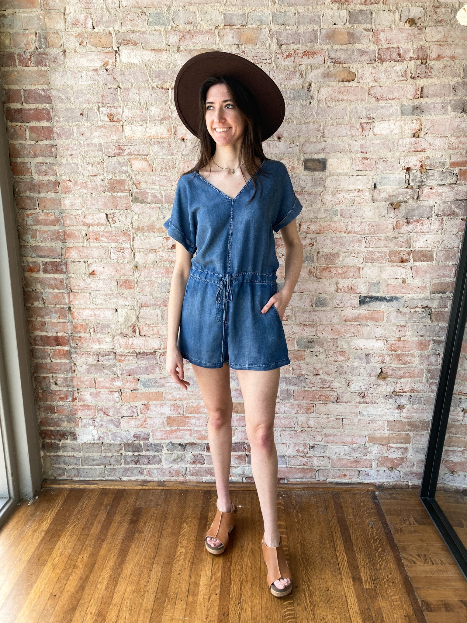 A young girl in her 30s wearing a denim romper and a big brown hat and platform shoes.