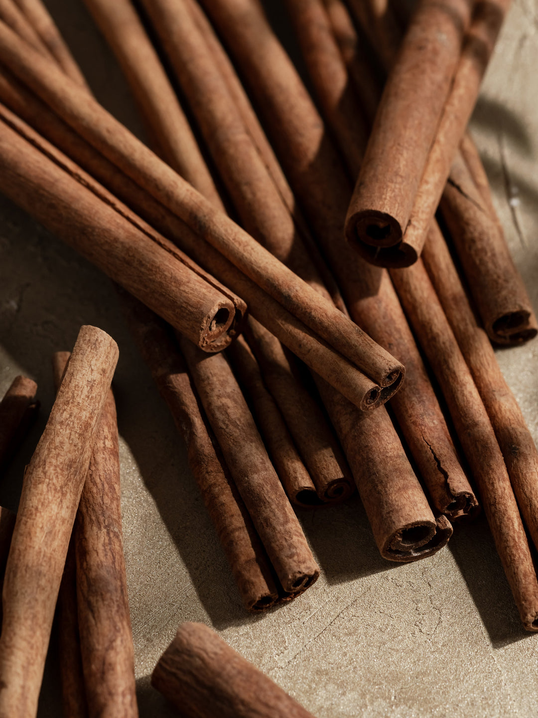 Close-up of multiple cinnamon sticks scattered on a light stone surface, ingredient shot for Pura Pumpkin Spice fragrance.