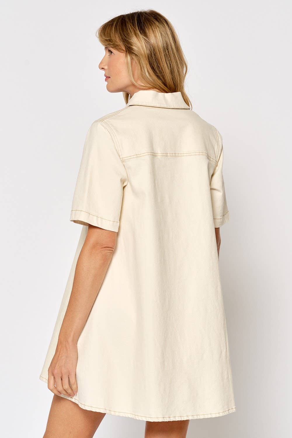 Woman wearing cream colored short sleeve button down shirt dress, back view