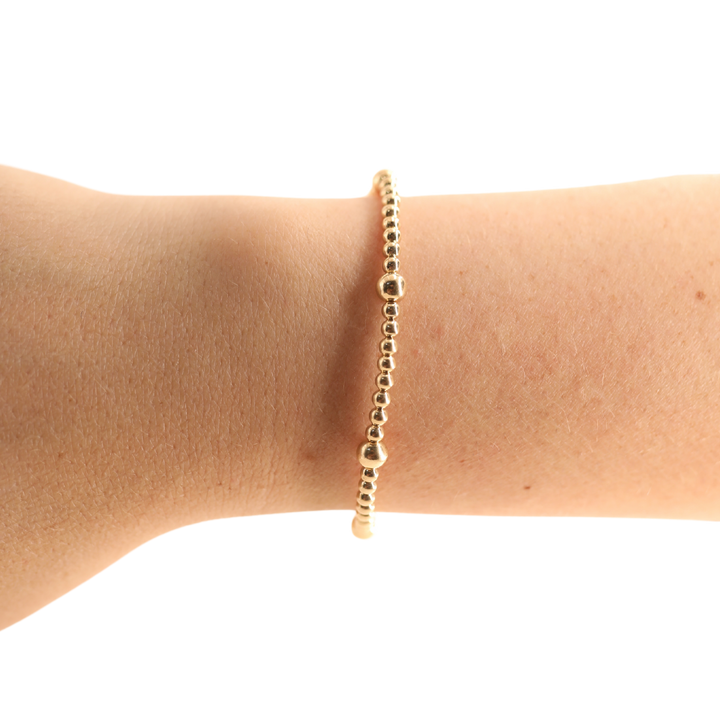 Beaded Blondes Olive Bracelet in gold beads worn on a wrist against black background