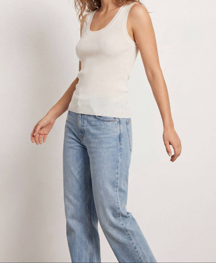 Woman wearing white ribbed knit tank top with blue jeans on white background