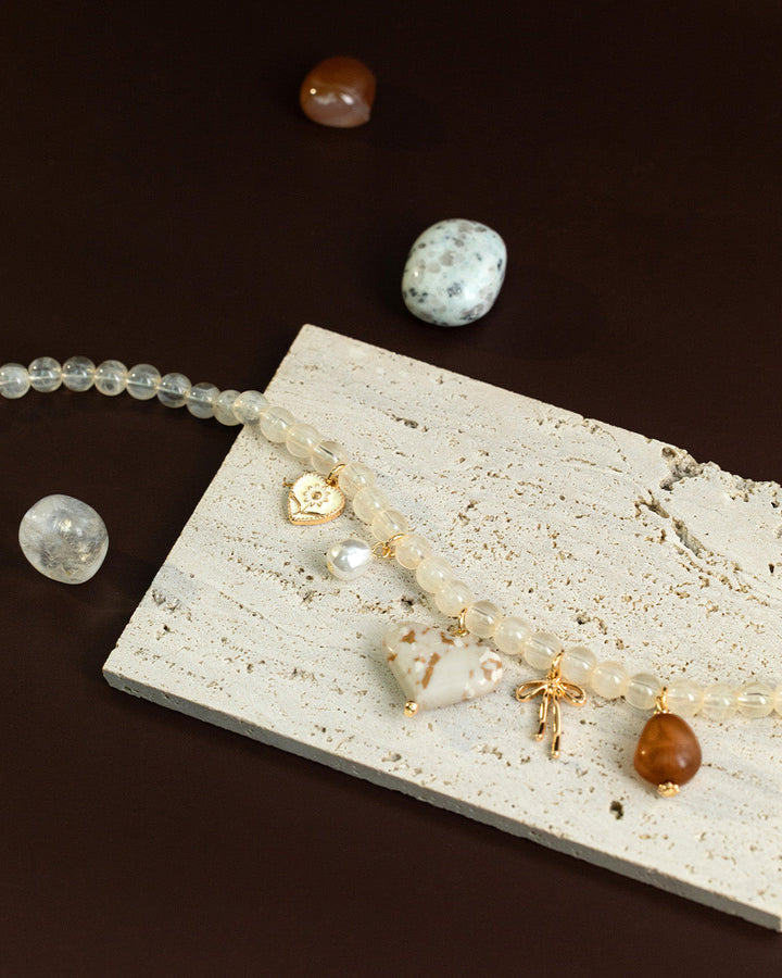 Ivory jade bead necklace with marbled white heart charm and gold pendants on stone surface