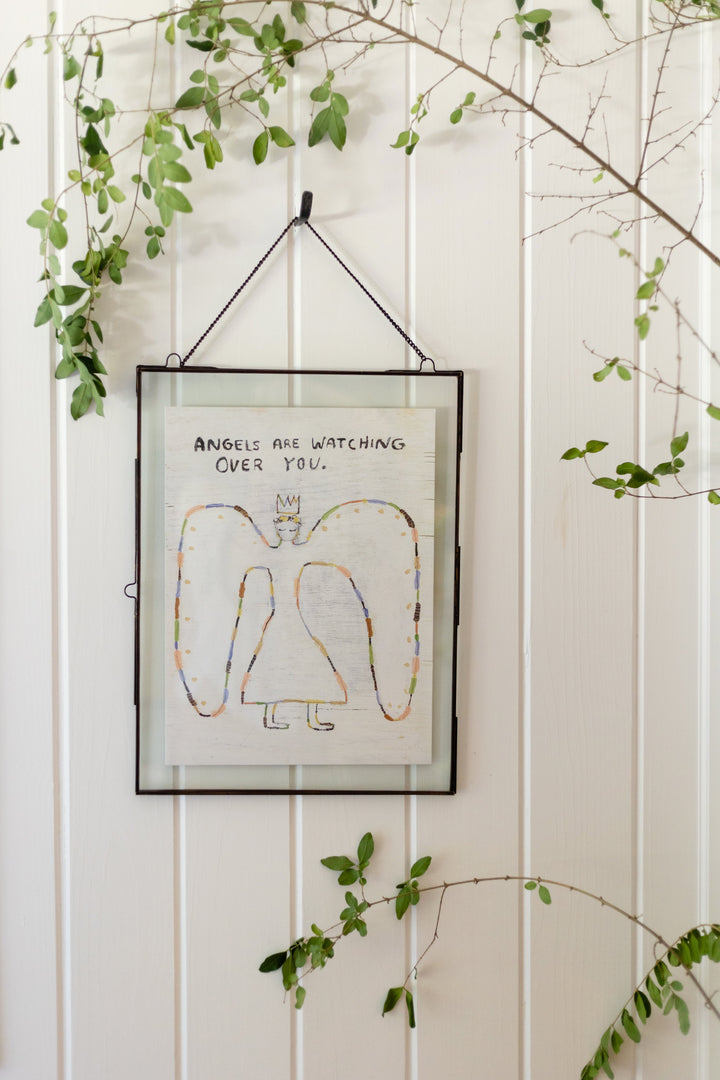 Framed art poster reading 'Angels Are Watching Over You' with colorful angel drawing