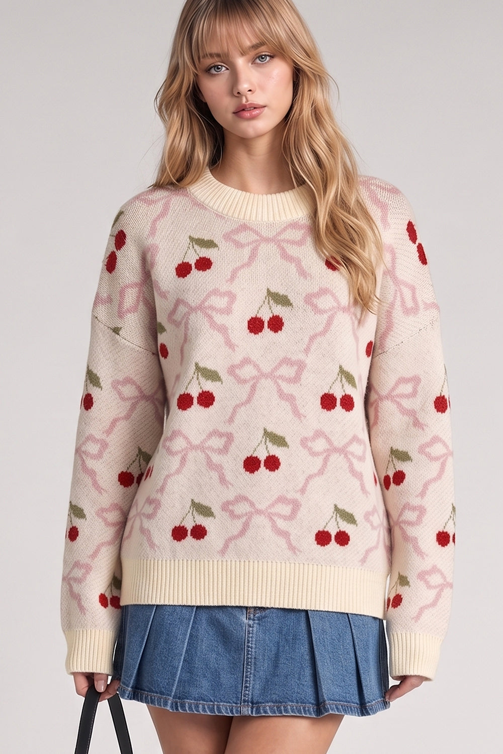 Cream knit sweater with red cherry and pink bow jacquard pattern, worn with denim mini skirt