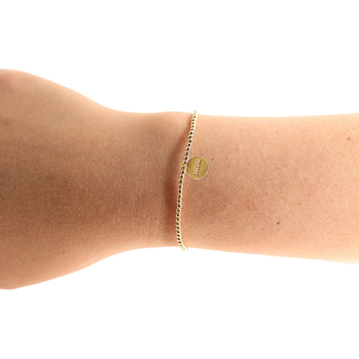 Gold beaded bracelet with small engraved Mom charm disc worn on wrist