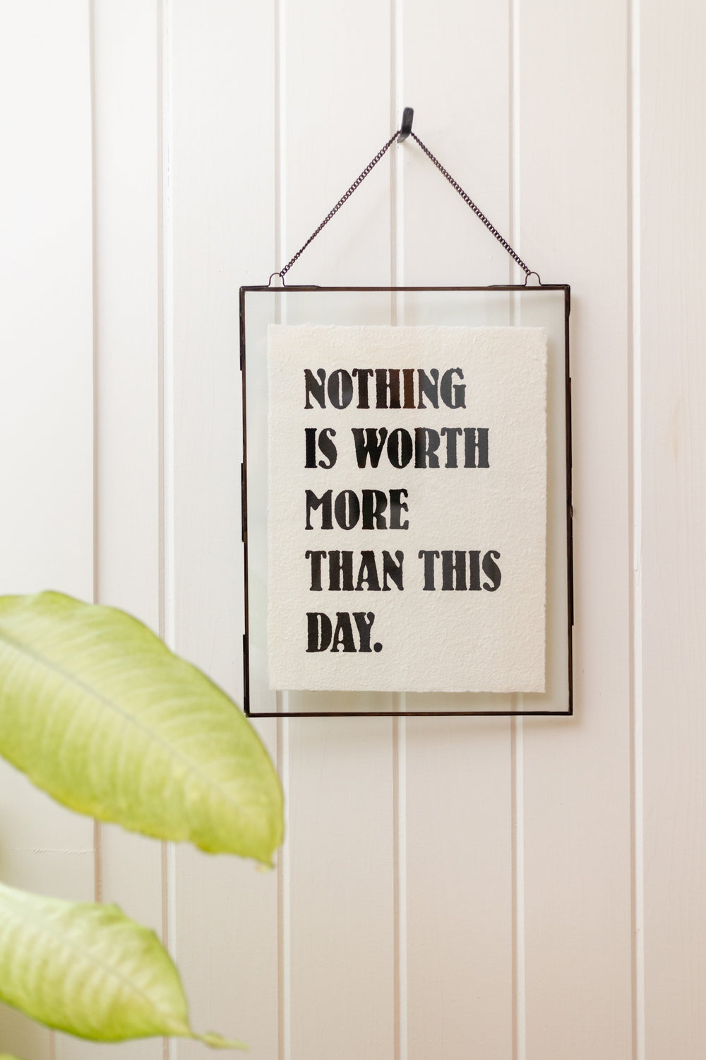 Framed handmade paper print reading 'Nothing Is Worth More Than This Day' hung on white wall
