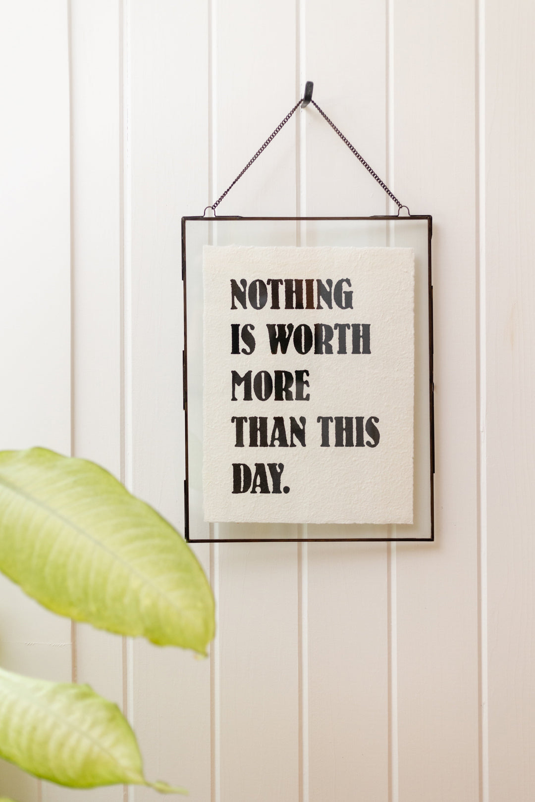 Framed handmade paper print reading 'Nothing Is Worth More Than This Day' hung on white wall