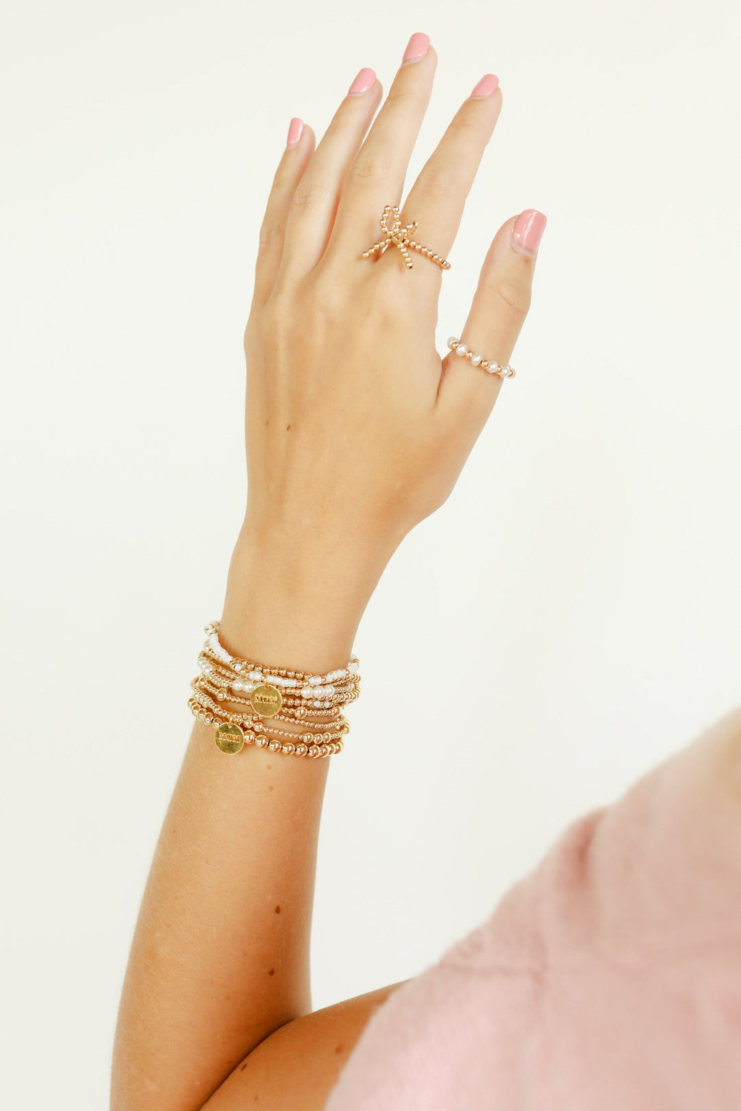 Stacked gold beaded bracelets with Mom charm disc worn on wrist with rings