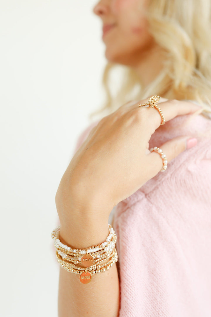 Woman wearing stacked gold beaded bracelets with MOM charm pendant on wrist