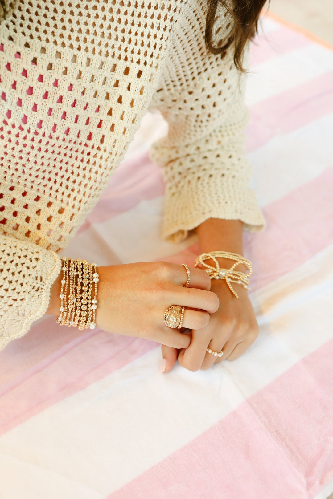 Gold beaded pearl bracelets stacked on wrist, styled with rings on striped surface.
