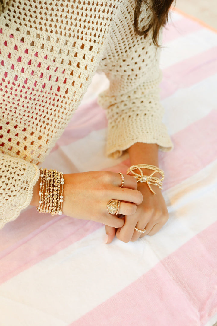 Gold beaded pearl bracelets stacked on wrist, styled with rings on striped surface.