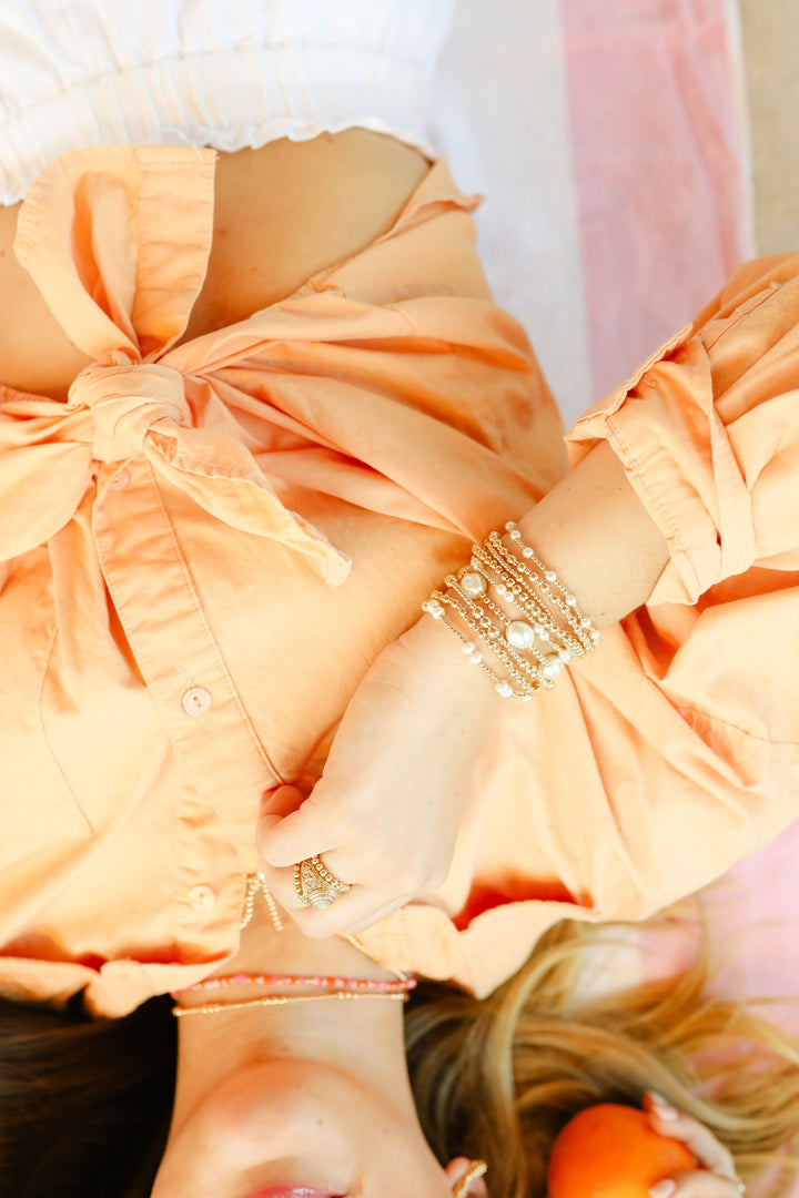 Stacked gold and pearl Leah Pearl Bracelet worn on wrist with peach outfit