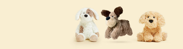 Three Warmies heated stuffed animal dogs in different colors on cream background