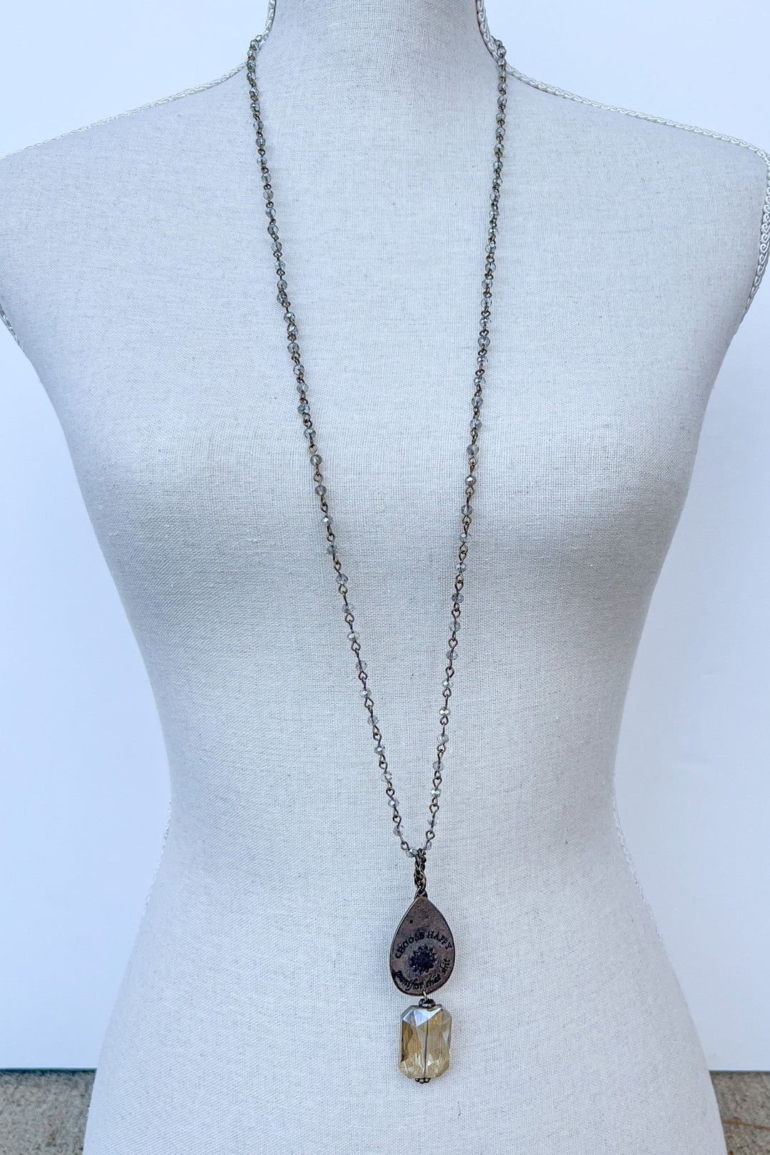 Choose Happy bronze necklace with teardrop charm and faceted crystal pendant on mannequin