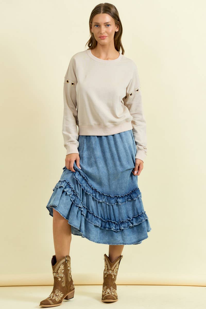 Woman wearing denim asymmetrical ruffle midi skirt with tiered fringe details and neutral sweatshirt