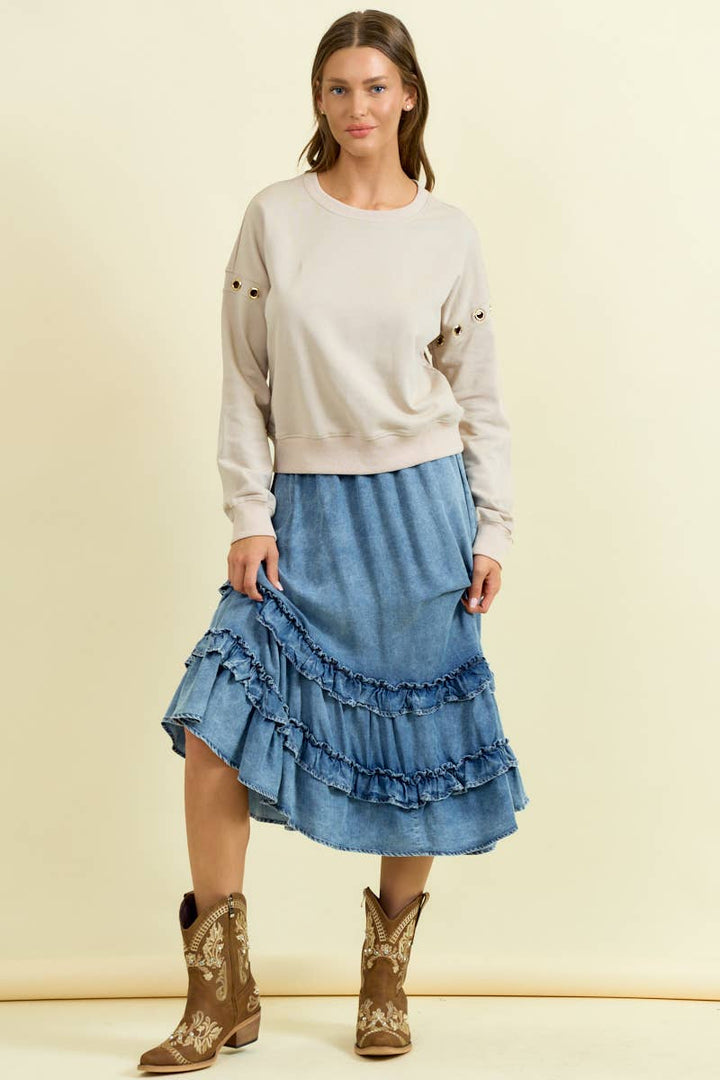 Woman wearing denim asymmetrical ruffle midi skirt with tiered fringe details and neutral sweatshirt