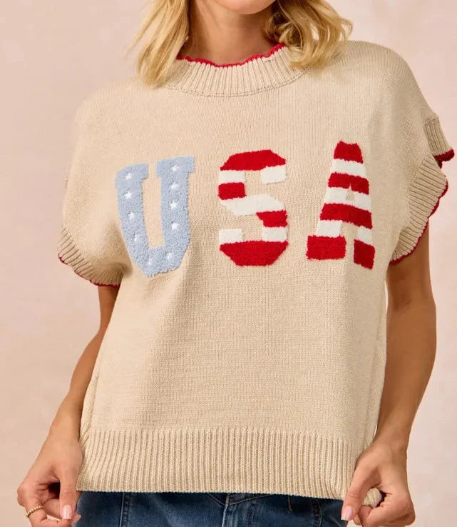 Woman wearing oatmeal knit sweater vest with patriotic USA lettering in red and blue