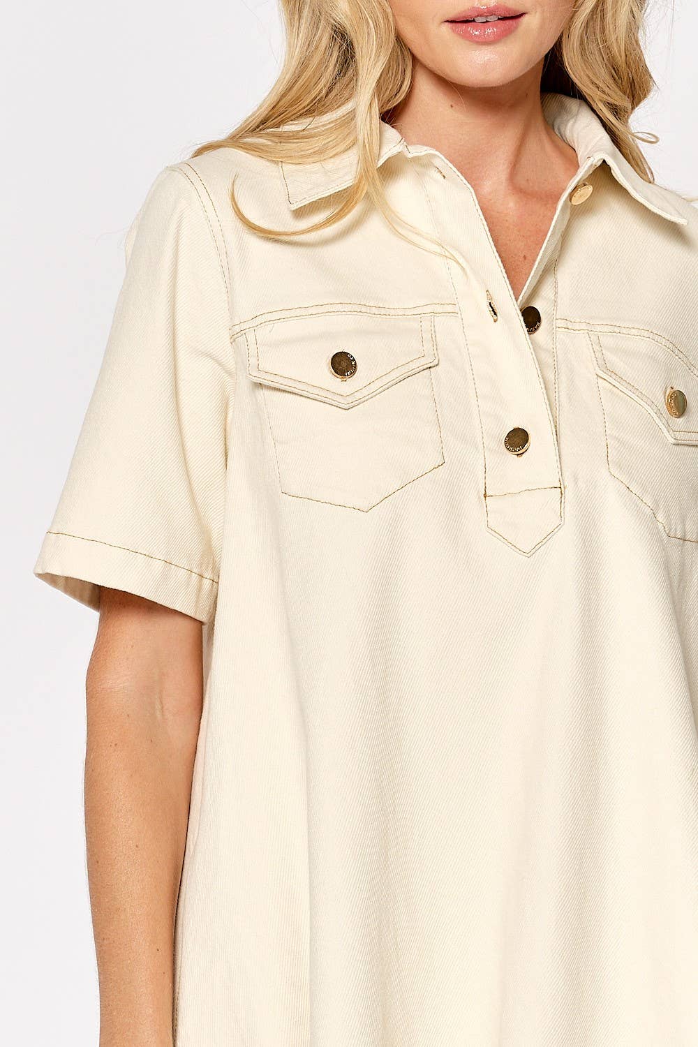 Woman wearing cream colored short sleeve button down shirt dress with chest pockets