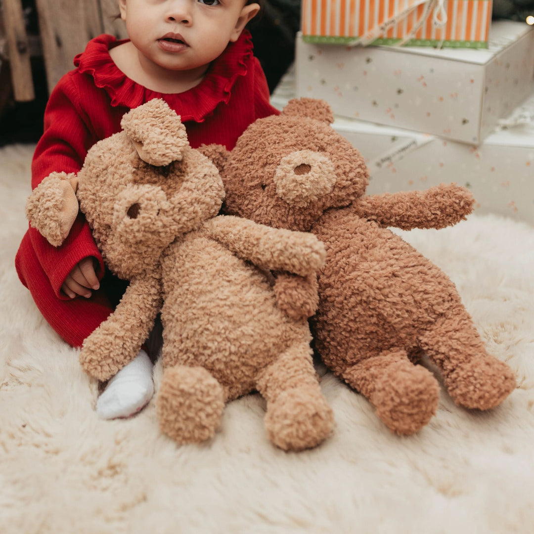 Toddler in red dress holding two Brownie The Bear plush teddy bears on fur rug