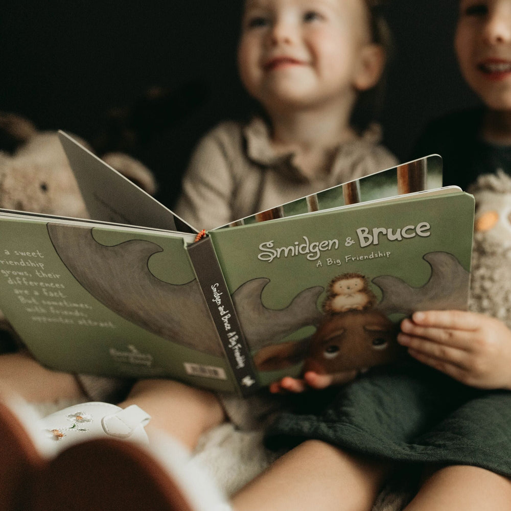 Children holding open Smidgen and Bruce A Big Friendship board book with green illustrated cover