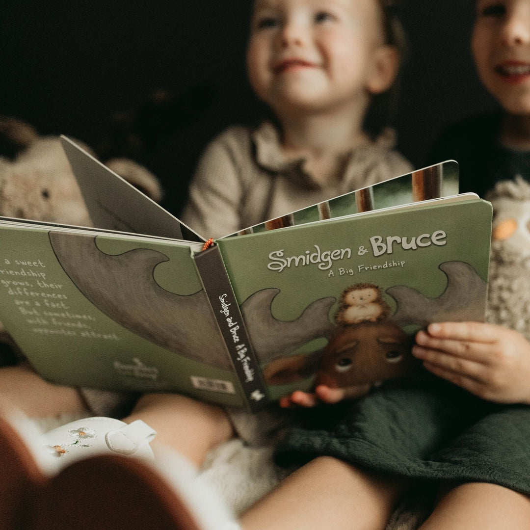 Children holding open Smidgen and Bruce A Big Friendship board book with green illustrated cover