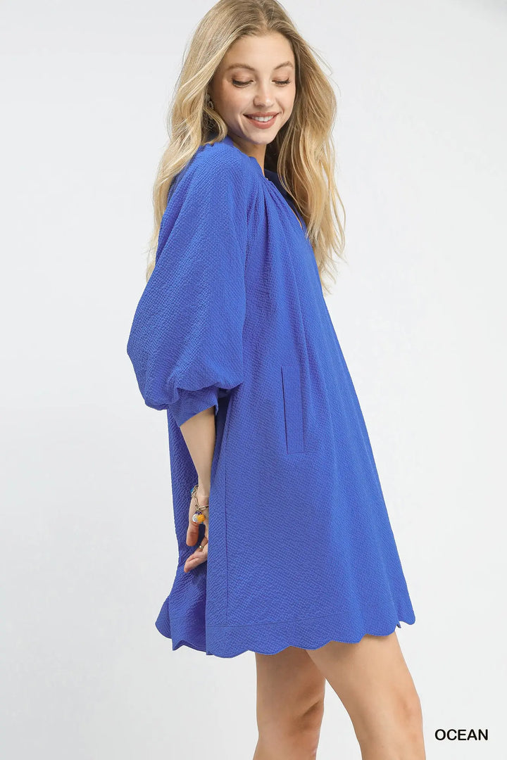 Woman wearing bright blue textured mini dress with three-quarter sleeves and pockets