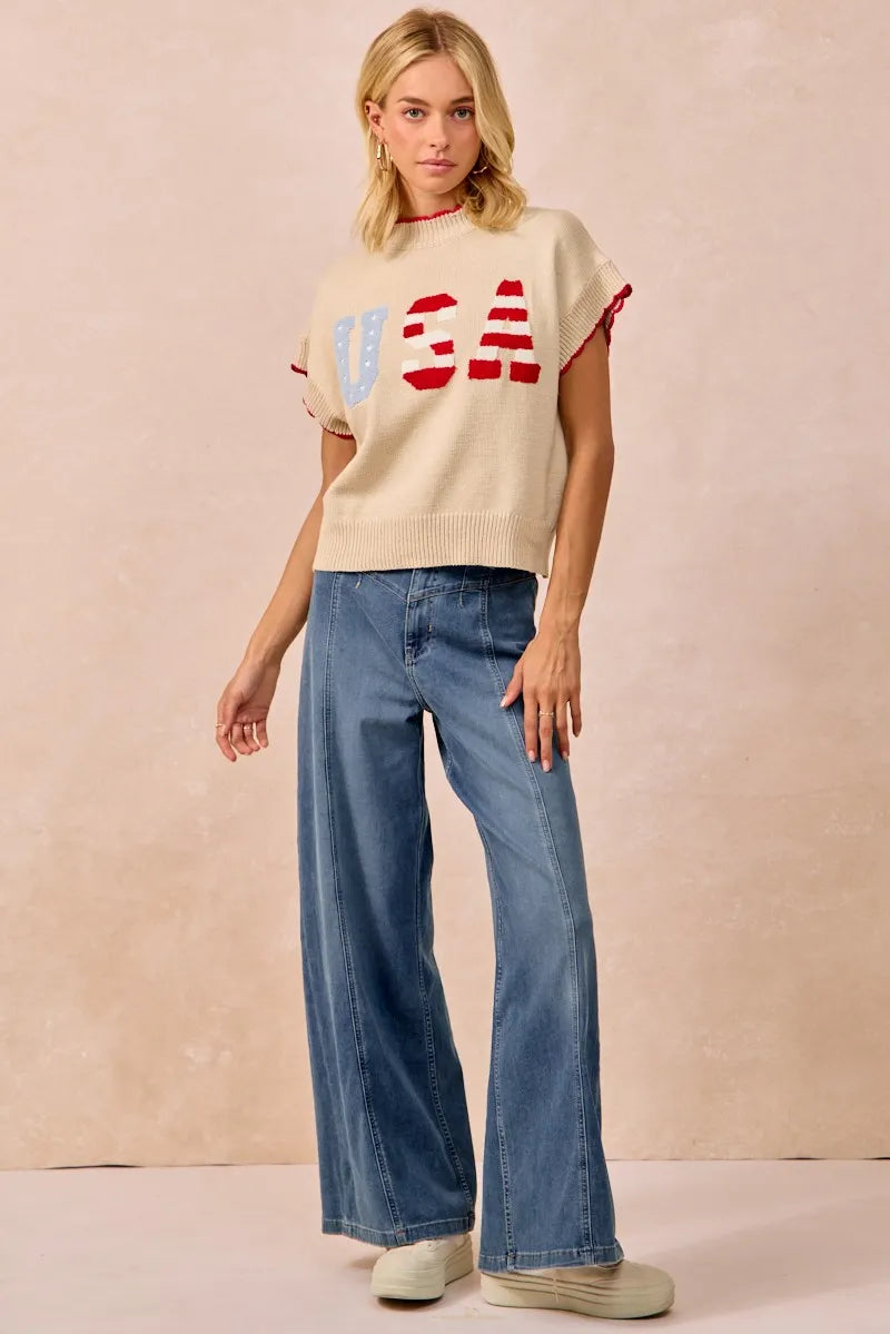 Woman wearing oatmeal colored sleeveless sweater vest with red and white USA lettering