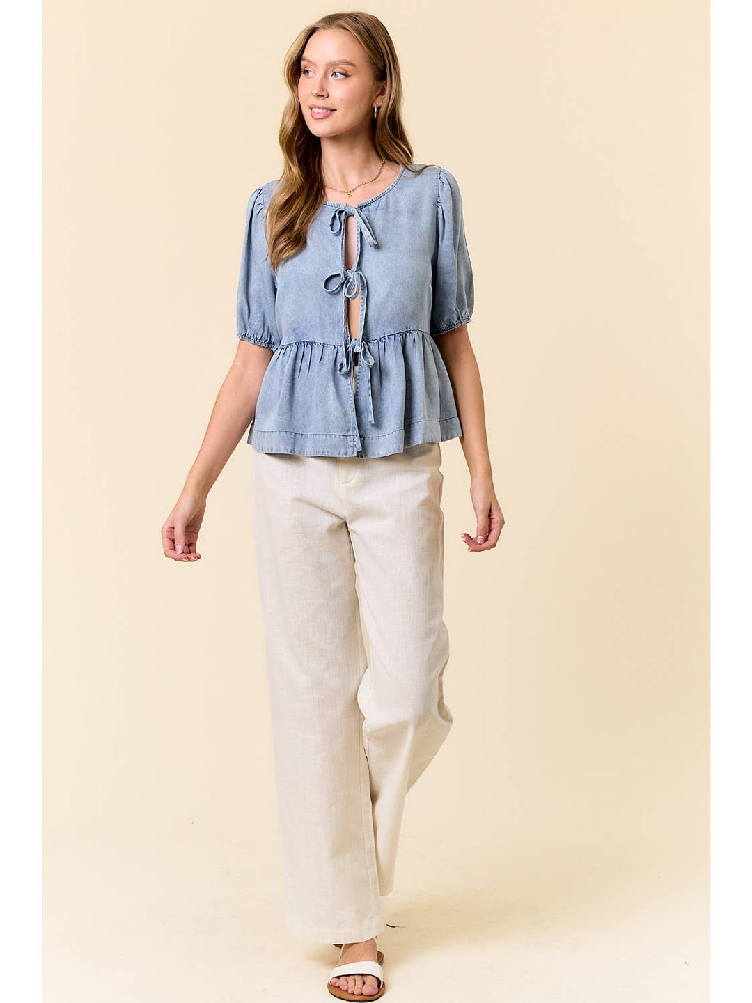 Woman wearing light blue chambray peplum top with tie-front detail and cream pants