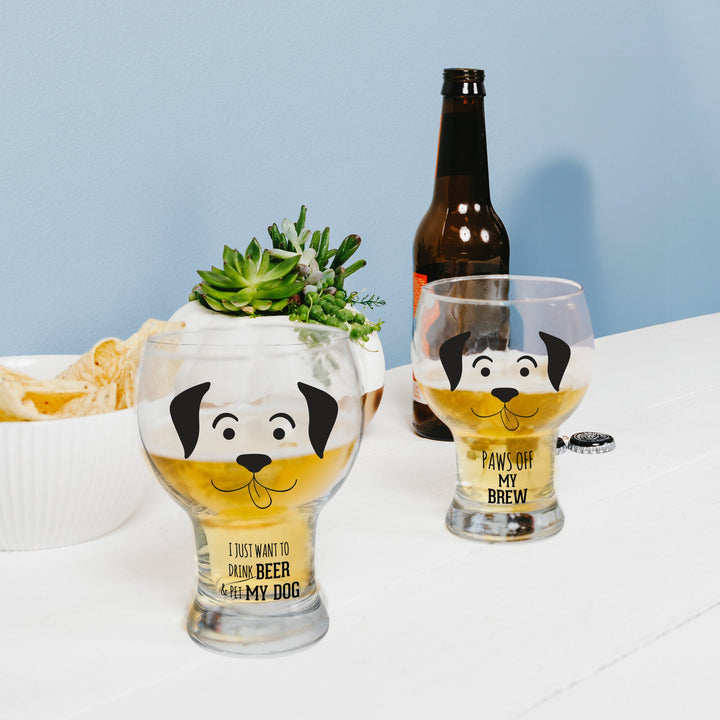 Two dog-themed pilsner glasses with cute black dog faces, filled with golden beer