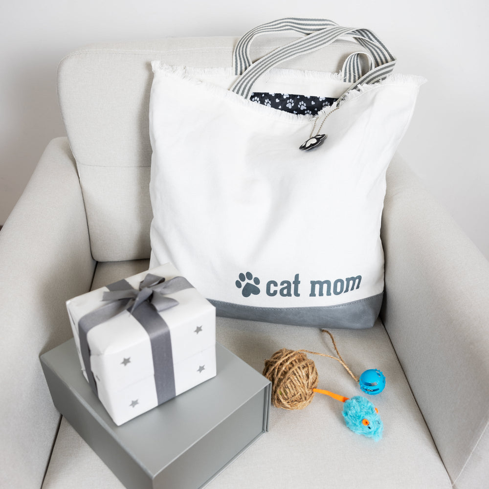 White canvas tote bag with cat mom text and paw print design on chair