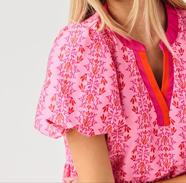Woman wearing pink mini dress with red floral vine pattern and contrasting collar trim