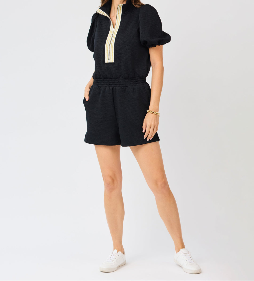 Woman wearing black Andie romper with gold trim detail and puffed sleeves