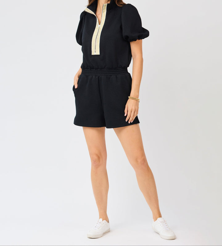 Woman wearing black Andie romper with gold trim detail and puffed sleeves
