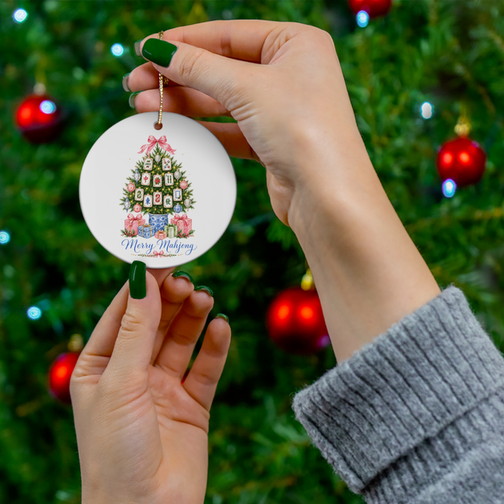 Hands holding a round ceramic Merry Mahjong Christmas ornament with mahjong tile tree design