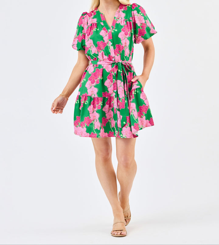 Woman wearing green dress with pink orchid floral print, short sleeves, tie waist