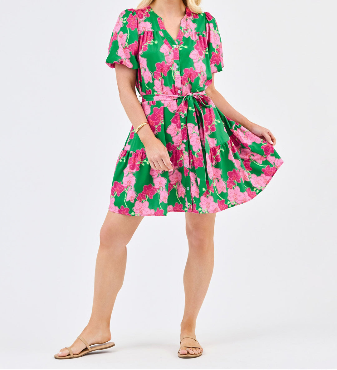 Woman wearing green dress with pink orchid floral print, short sleeves, button front, belted waist