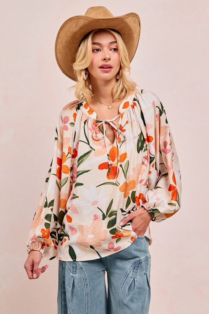 Woman wearing floral print balloon sleeve top with orange and pink flowers on cream background