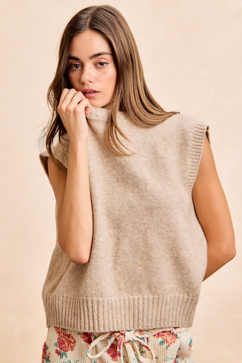 Woman wearing taupe sleeveless turtleneck knit vest with ribbed trim against neutral background