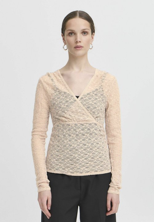 Woman wearing cream colored long-sleeve lace wrap top with V-neckline