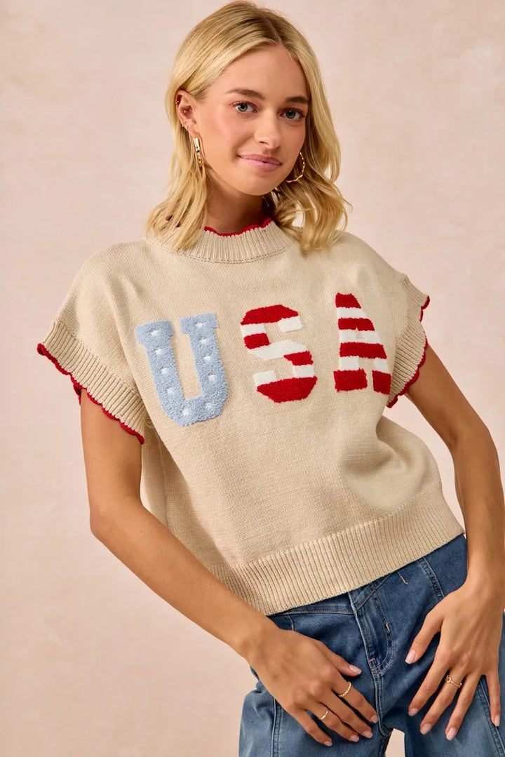 Woman wearing oatmeal USA patchwork sweater vest with blue and red lettering