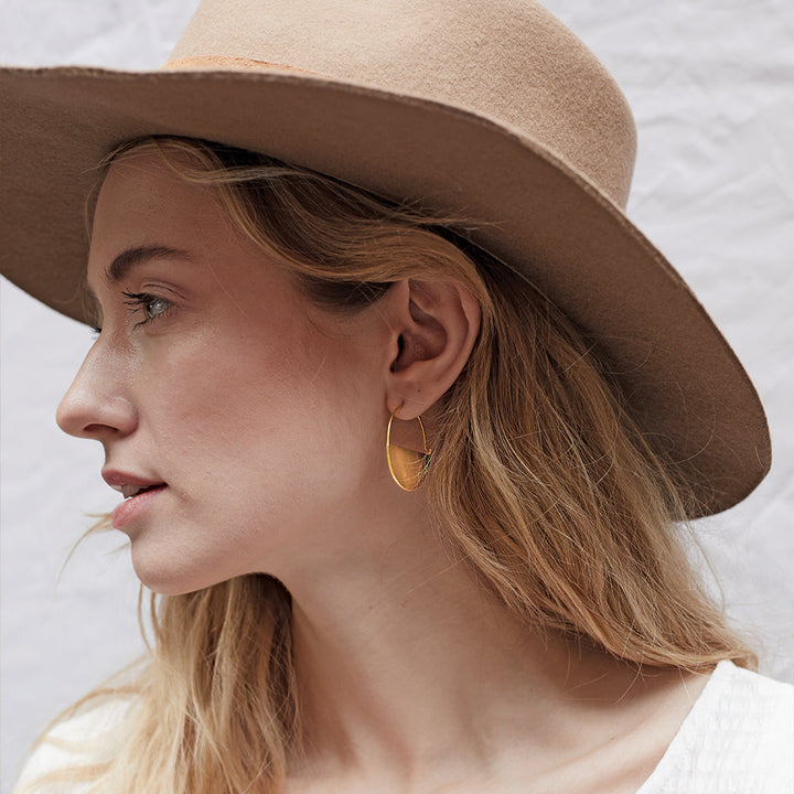 Model wearing Scout Refined Collection Lunar Hoop gold vermeil earring with wide-brim hat