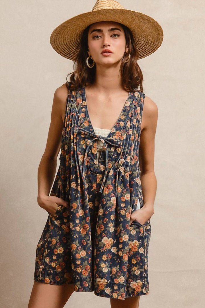 Woman wearing navy floral denim romper with tie-front detail and straw hat