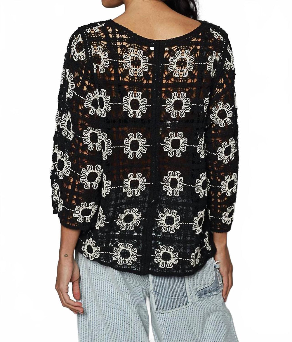 Black crochet cardigan with white daisy flower pattern worn over light blue pants