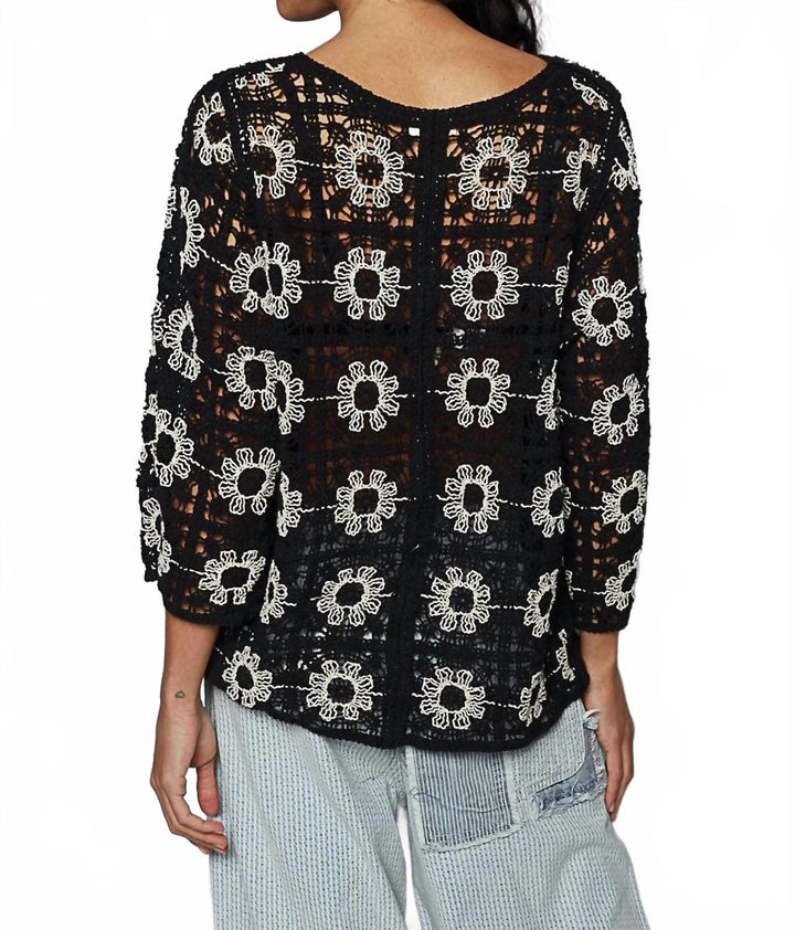 Black crochet cardigan with white daisy flower pattern worn over light blue pants