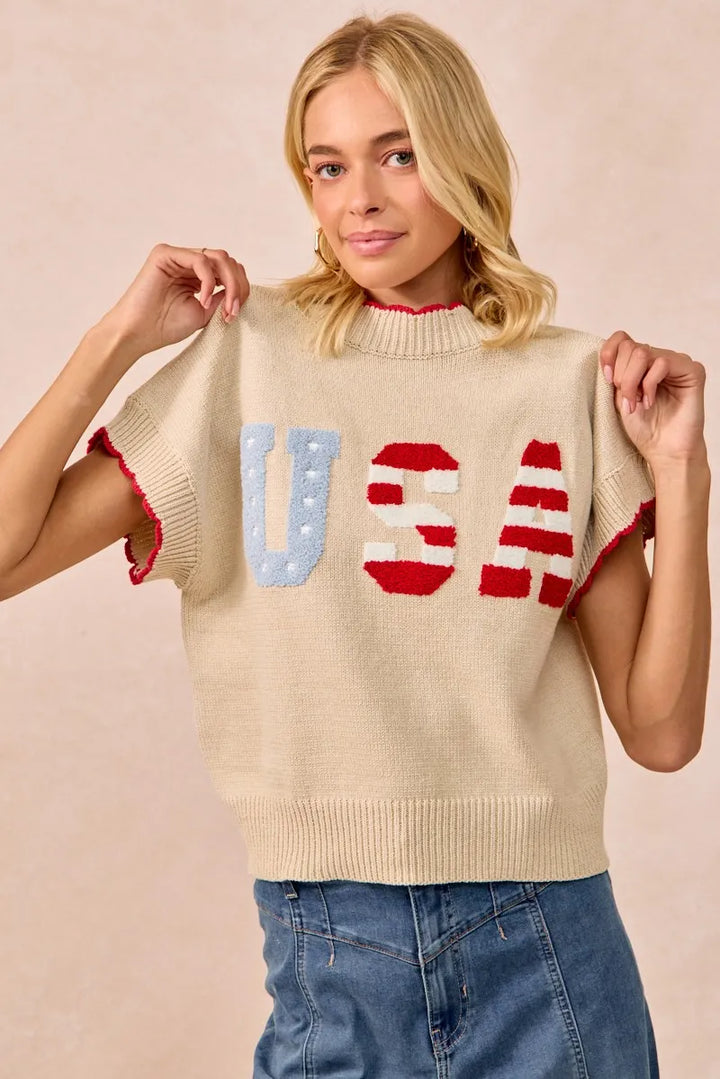 Woman wearing oatmeal knit sweater vest with red white blue USA lettering